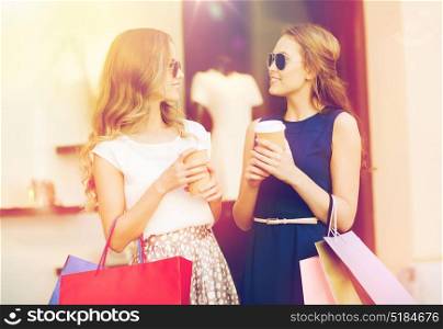 sale, consumerism and people concept - happy young women with shopping bags and coffee paper cups talking at shop window in city. young women with shopping bags and coffee at shop