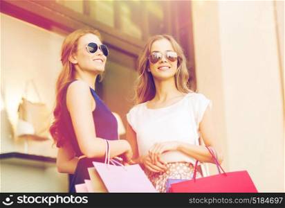 sale, consumerism and people concept - happy young women with shopping bags and coffee paper cups at shop window in city. young women with shopping bags and coffee at shop