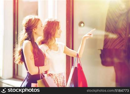 sale, consumerism and people concept - happy young women with shopping bags pointing finger to shop window in city. happy women with shopping bags at shop window
