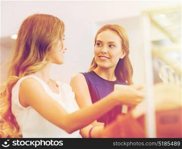 sale, consumerism and people concept - happy young women with shopping bags choosing clothes at clothing shop. happy women with shopping bags at clothing shop