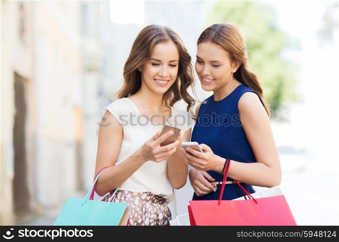 sale, consumerism and people concept - happy young women with shopping bags and smartphone on city street