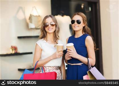 sale, consumerism and people concept - happy young women with shopping bags and coffee paper cups at shop window in city