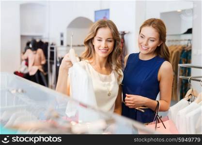 sale, consumerism and people concept - happy young women with shopping bags choosing clothes at clothing shop