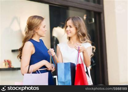 sale, consumerism and people concept - happy young women with shopping bags talking at shop window in city