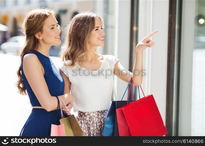 sale, consumerism and people concept - happy young women with shopping bags pointing finger to shop window in city