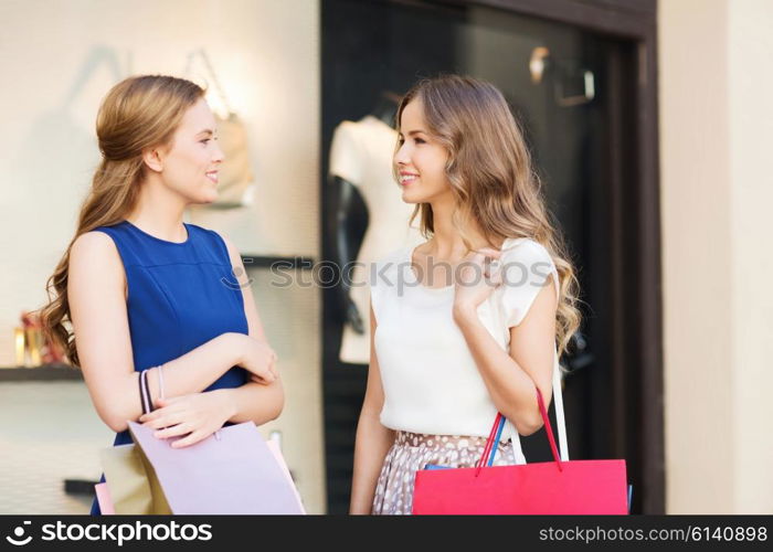 sale, consumerism and people concept - happy young women with shopping bags talking at shop window in city