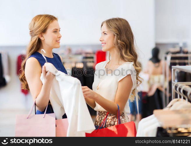 sale, consumerism and people concept - happy young women with shopping bags choosing clothes at clothing shop