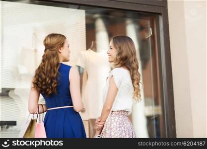 sale, consumerism and people concept - happy young women with shopping bags talking at to shop window in city from back