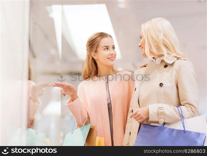 sale, consumerism and people concept - happy young women with shopping bags pointing finger to window in mall