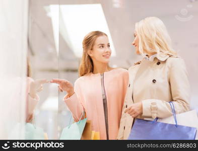 sale, consumerism and people concept - happy young women with shopping bags pointing finger to window in mall