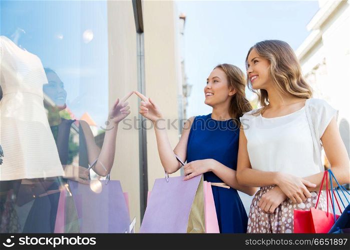 sale, consumerism and people concept - happy young women with shopping bags pointing finger to dress at storefront. happy women with shopping bags at storefront