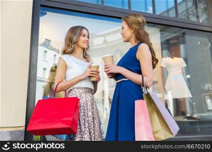 sale, consumerism and people concept - happy young women with shopping bags and coffee takeout at storefront. happy women with shopping bags and coffee outdoors. happy women with shopping bags and coffee outdoors