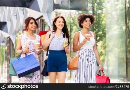 sale, consumerism and people concept - happy young women with shopping bags and drinks walking along city street. women with shopping bags and drinks in city