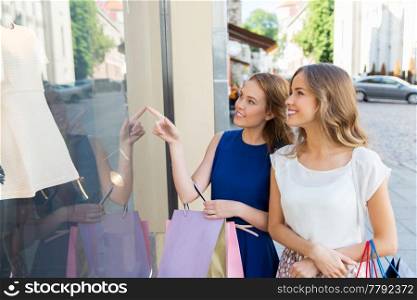 sale, consumerism and people concept - happy young women with shopping bags pointing finger to dress at storefront. happy women with shopping bags at storefront