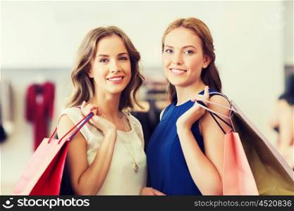 sale, consumerism and people concept - happy young women with shopping bags at clothing shop