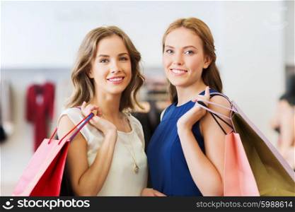 sale, consumerism and people concept - happy young women with shopping bags at clothing shop