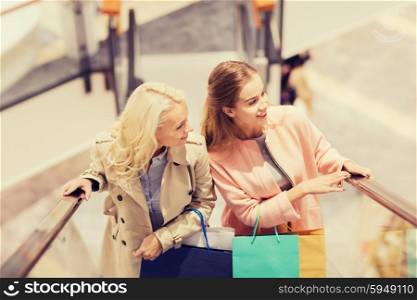 sale, consumerism and people concept - happy young women with shopping bags on escalator in mall