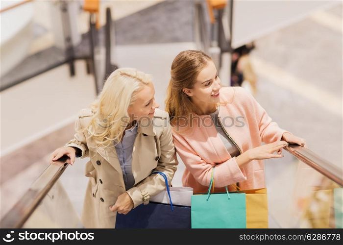 sale, consumerism and people concept - happy young women with shopping bags on escalator in mall