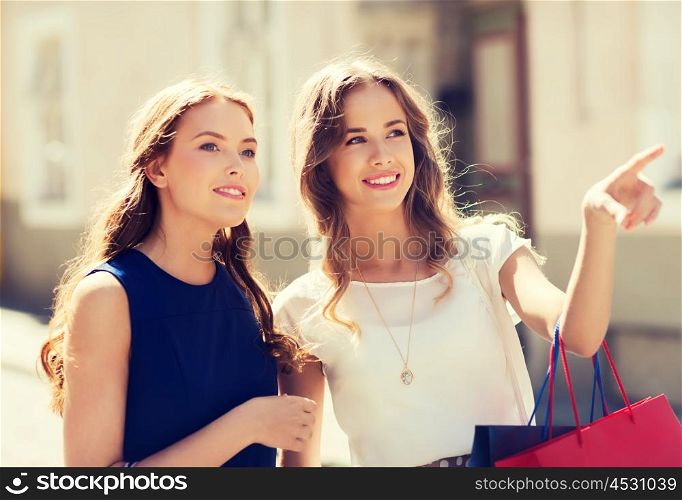 sale, consumerism and people concept - happy young women with shopping bags pointing finger in city