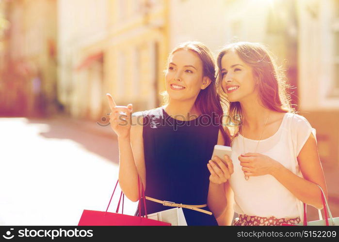 sale, consumerism and people concept - happy young women with shopping bags pointing finger in city. happy women with shopping bags in city