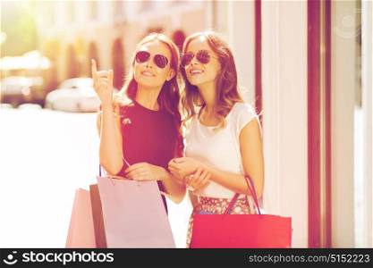 sale, consumerism and people concept - happy young women with shopping bags pointing finger in city. happy women with shopping bags in city