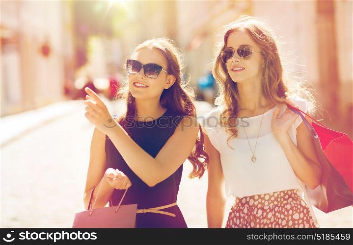 sale, consumerism and people concept - happy young women with shopping bags pointing finger in city. happy women with shopping bags in city