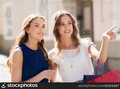 sale, consumerism and people concept - happy young women with shopping bags pointing finger in city