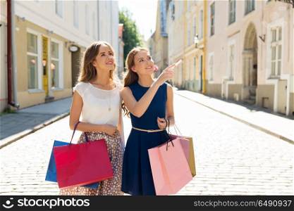 sale, consumerism and people concept - happy young women with shopping bags pointing finger in city. happy women with shopping bags in city. happy women with shopping bags in city
