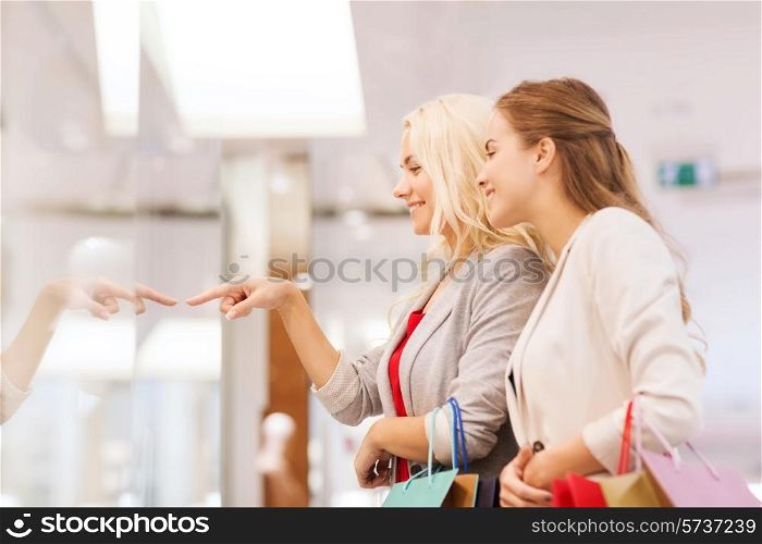 sale, consumerism and people concept - happy young women with shopping bags pointing finger in mall
