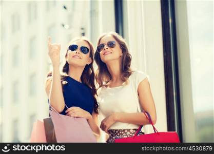sale, consumerism and people concept - happy young women with shopping bags pointing finger outdoors