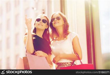 sale, consumerism and people concept - happy young women with shopping bags pointing finger outdoors. happy women with shopping bags outdoors