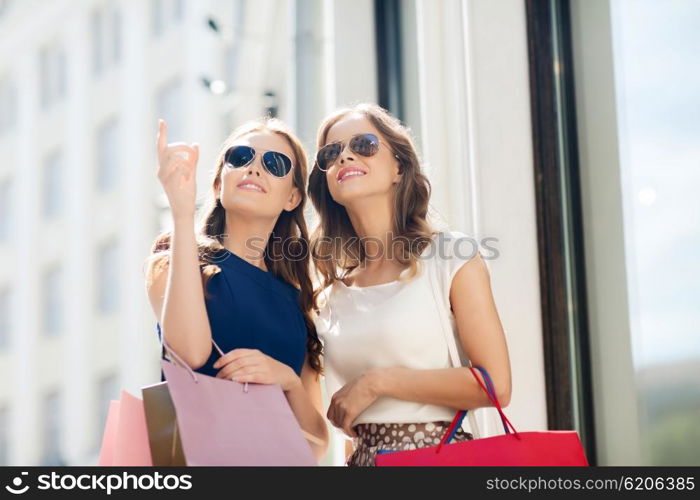 sale, consumerism and people concept - happy young women with shopping bags pointing finger outdoors