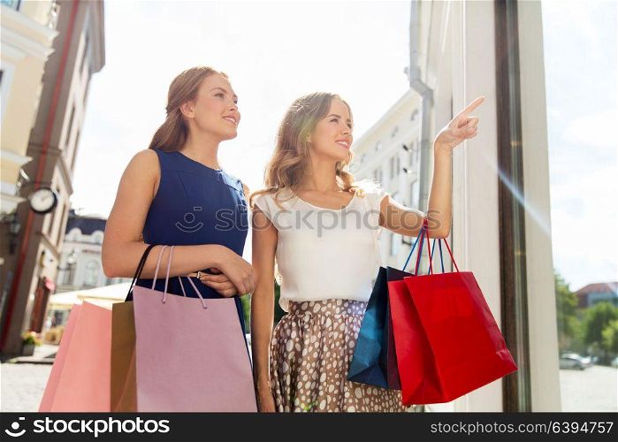 sale, consumerism and people concept - happy young women with shopping bags pointing finger to storefront. happy women with shopping bags at storefront