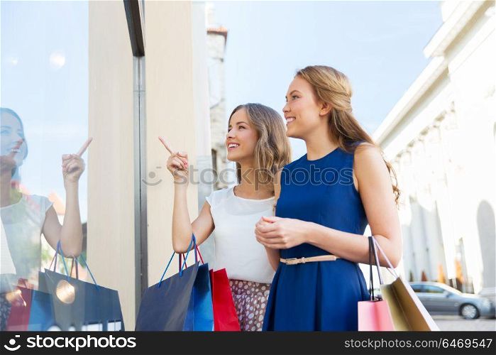 sale, consumerism and people concept - happy young women with shopping bags pointing finger to storefront. happy women with shopping bags at storefront