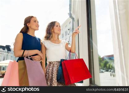 sale, consumerism and people concept - happy young women with shopping bags pointing finger to storefront. happy women with shopping bags at storefront. happy women with shopping bags at storefront