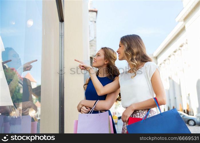 sale, consumerism and people concept - happy young women with shopping bags pointing finger to storefront. happy women with shopping bags at storefront. happy women with shopping bags at storefront