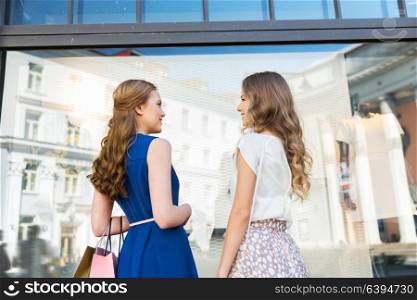 sale, consumerism and people concept - happy young women with shopping bags talking at storefront. happy women with shopping bags at storefront