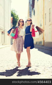 sale, consumerism and people concept - happy young women with shopping bags walking along city street