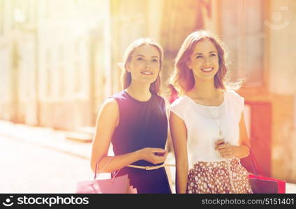 sale, consumerism and people concept - happy young women with shopping bags walking along city street. happy women with shopping bags walking in city