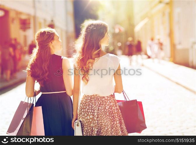 sale, consumerism and people concept - happy young women with shopping bags walking along city street. happy women with shopping bags walking in city