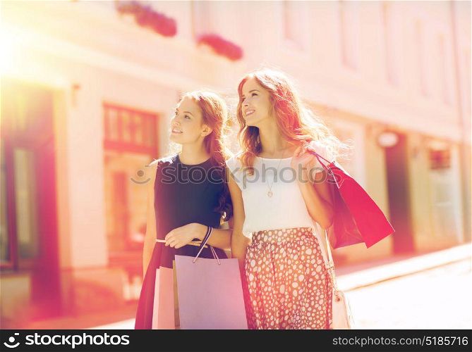 sale, consumerism and people concept - happy young women with shopping bags walking along city street. happy women with shopping bags walking in city