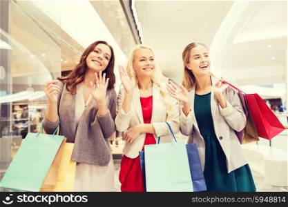 sale, consumerism and people concept - happy young women with shopping bags waving hands in mall