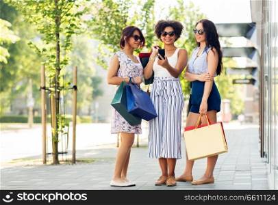 sale, consumerism and people concept - happy young women with smartphones and shopping bags on city street. women with smartphones and shopping bags in city
