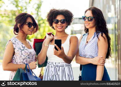 sale, consumerism and people concept - happy young women with smartphones and shopping bags on city street. women with smartphones and shopping bags in city