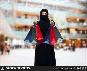 sale, consumerism and people concept - muslim woman in hijab with shopping bags over shopping center background. muslim woman in hijab with shopping bags