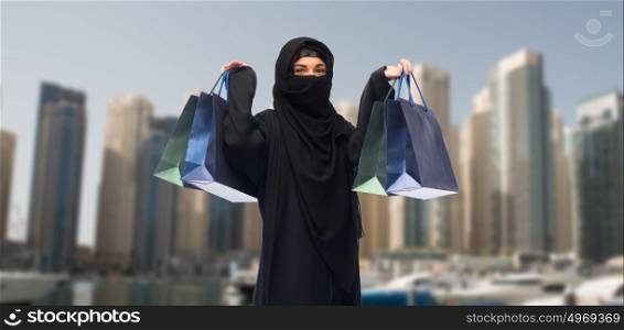 sale, consumerism and people concept - muslim woman in hijab with shopping bags over dubai city street background. muslim woman in hijab with shopping bags in dubai