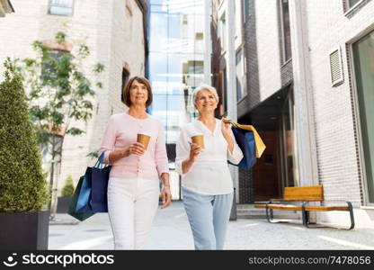 sale, consumerism and people concept - two senior women or friends with shopping bags drinking takeaway coffee and walking along tallinn city street. senior women with shopping bags and coffee in city