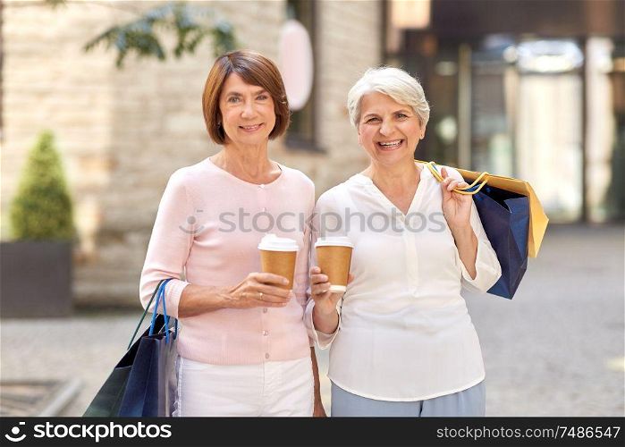 sale, consumerism and people concept - two senior women or friends with shopping bags drinking takeaway coffee on tallinn city street. senior women with shopping bags and coffee in city
