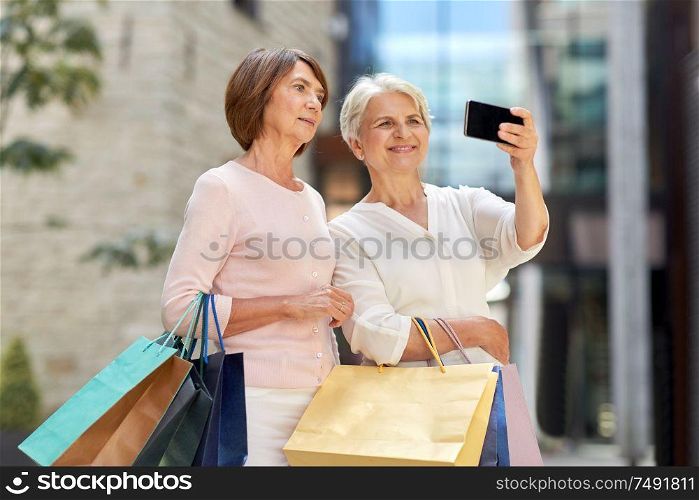 sale, consumerism and people concept - two senior women or friends with shopping bags taking selfie by smartphone on tallinn city street. old women with shopping bags taking selfie in city