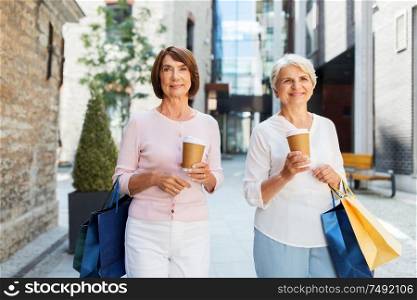 sale, consumerism and people concept - two senior women or friends with shopping bags drinking takeaway coffee and walking along tallinn city street. senior women with shopping bags and coffee in city